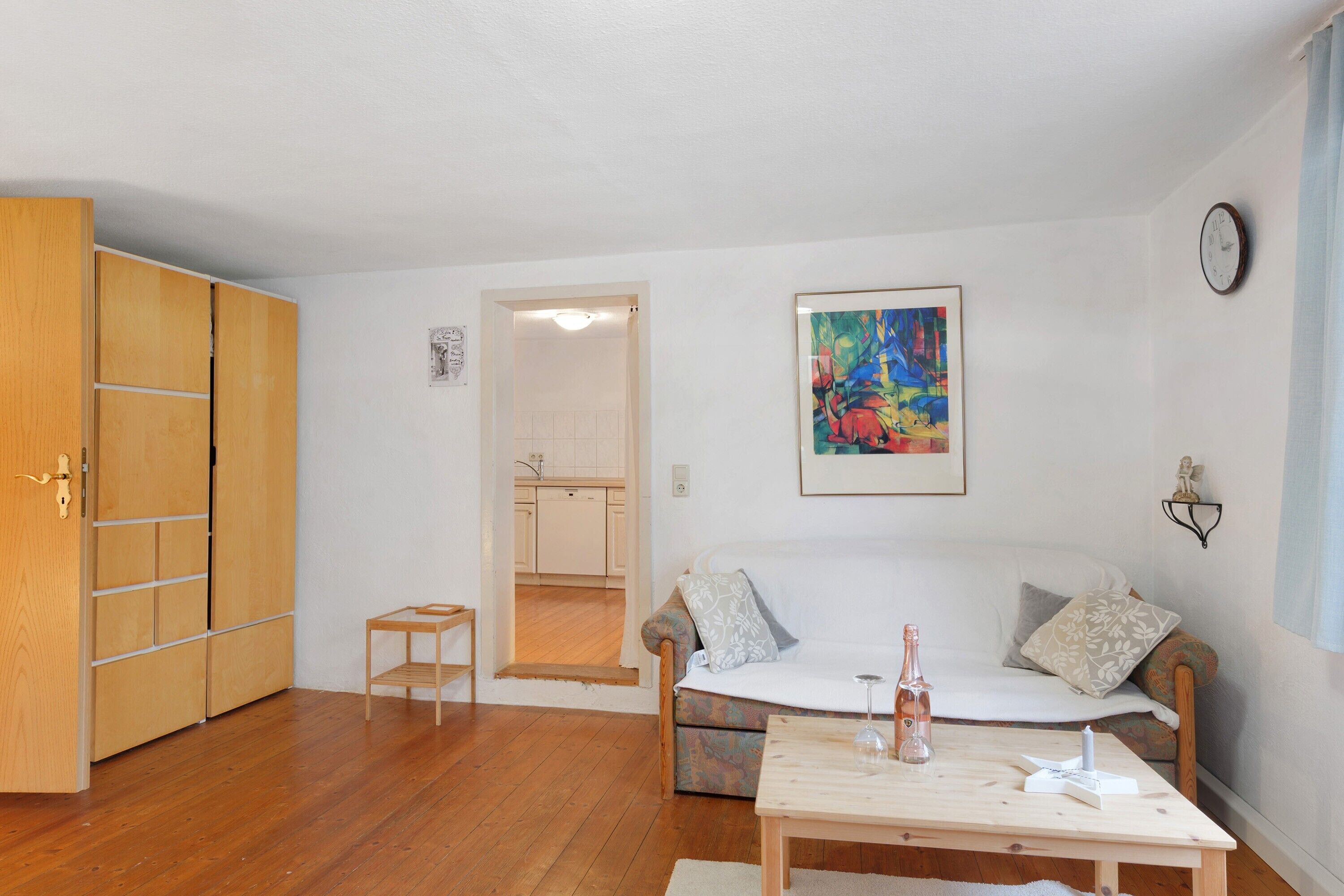 Un salon avec un canapé, une petite table, un meuble en bois et, au fond, une cuisine.
