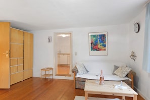 A living room with a sofa, a small table, a wooden cabinet, and a kitchen in the background. - Apartment 'Ferienwohnung 2' with Private Garden and Wi-Fi (Sternenfels)