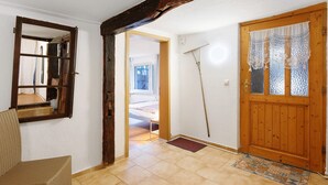 Un pasillo con puerta de madera, un espejo y una silla de mimbre.