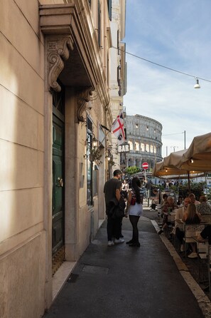 Eine Straße mit einem Café, Außenplätzen und einem historischen Gebäude im Hintergrund.