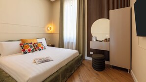 A hotel room with a bed, a nightstand, a lamp, a mirror, and a window with curtains. - DEZA Colosseum view (Roma)