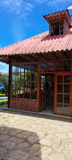 Un edificio rústico con techo de lámina corrugada, amplios ventanales y base de ladrillo.