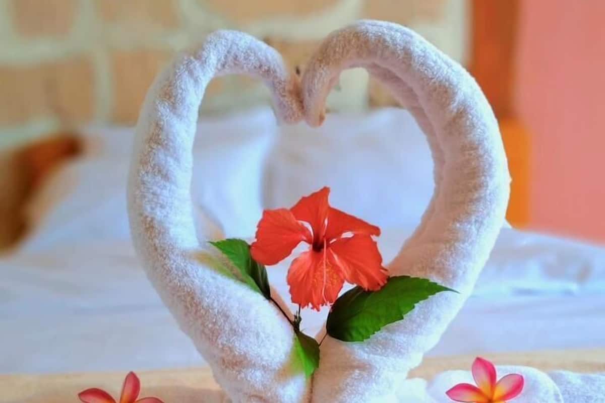 A bed with a heart-shaped towel arrangement featuring red flowers.
