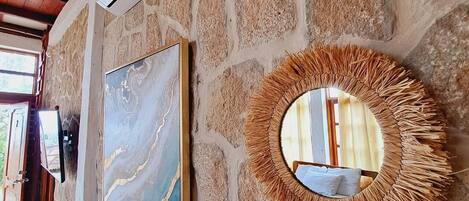 A stone wall with a framed painting and a mirror with a straw-like border.