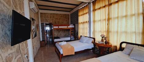 A room with bunk beds, a flat bed, a TV, and a small table with a lamp.