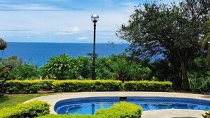 Una piscina rodeada de exuberante vegetación, con vistas despejadas al océano y un techo de tejas tradicionales.