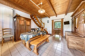 A wooden dining area with a table set for four, a bench, a wooden chair, a staircase, and a television mounted on the wall.
