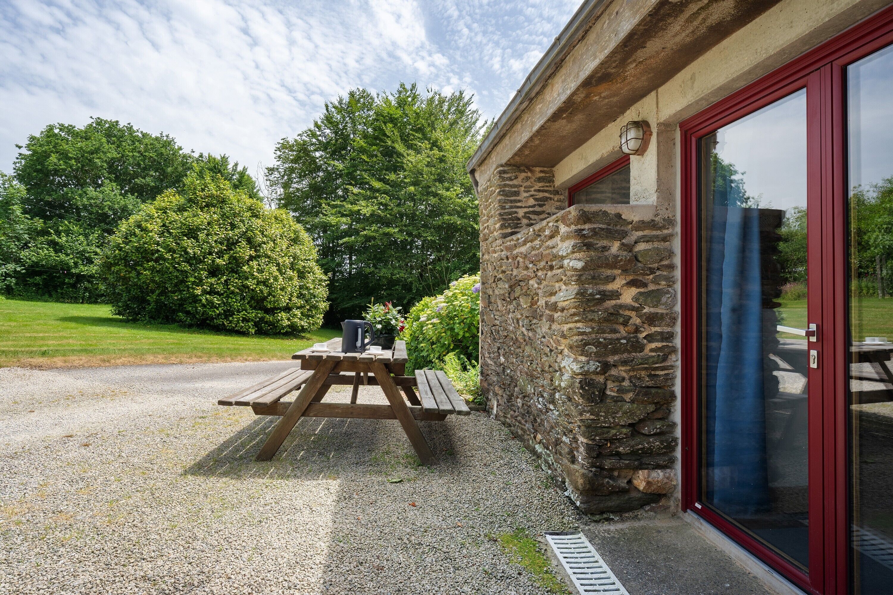 A stone building with a red door and a wooden picnic table outside.