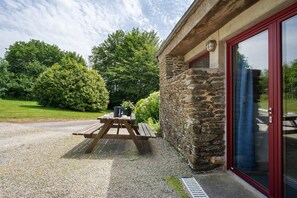 Un bâtiment en pierre avec une porte rouge et une table de pique-nique en bois à l’extérieur.