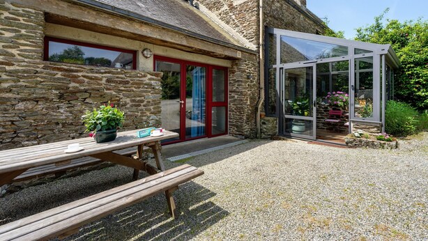 A stone building with a glass conservatory, a wooden bench, and a potted plant. - Holiday Home “Petit Gîte - Créac'h-Gourlès” with Wi-Fi (Plouvorn)