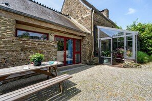 Un bâtiment en pierre doté d’une véranda en verre, d’un banc en bois et d’une plante en pot.