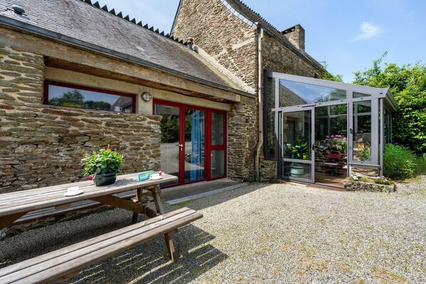 A stone building with a glass conservatory, a wooden bench, and a potted plant.