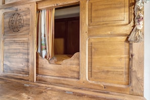 A wooden room with a bed, a window with curtains, and a decorative tassel.