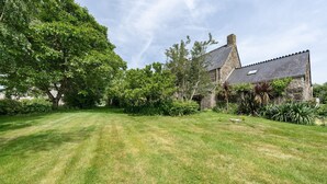 A stone house with a sloped roof, surrounded by a well-maintained lawn and various trees. - Holiday Home “Petit Gîte - Créac'h-Gourlès” with Wi-Fi (Plouvorn)
