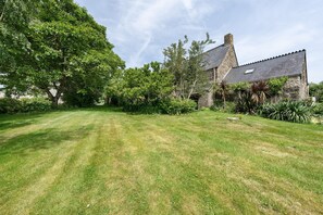 A stone house with a sloped roof, surrounded by a well-maintained lawn and various trees.