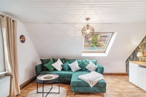 Et hyggeligt loftværelse med skråvægge, en grøn sofa med puder, et rundt sofabord og en hængende lampe.
