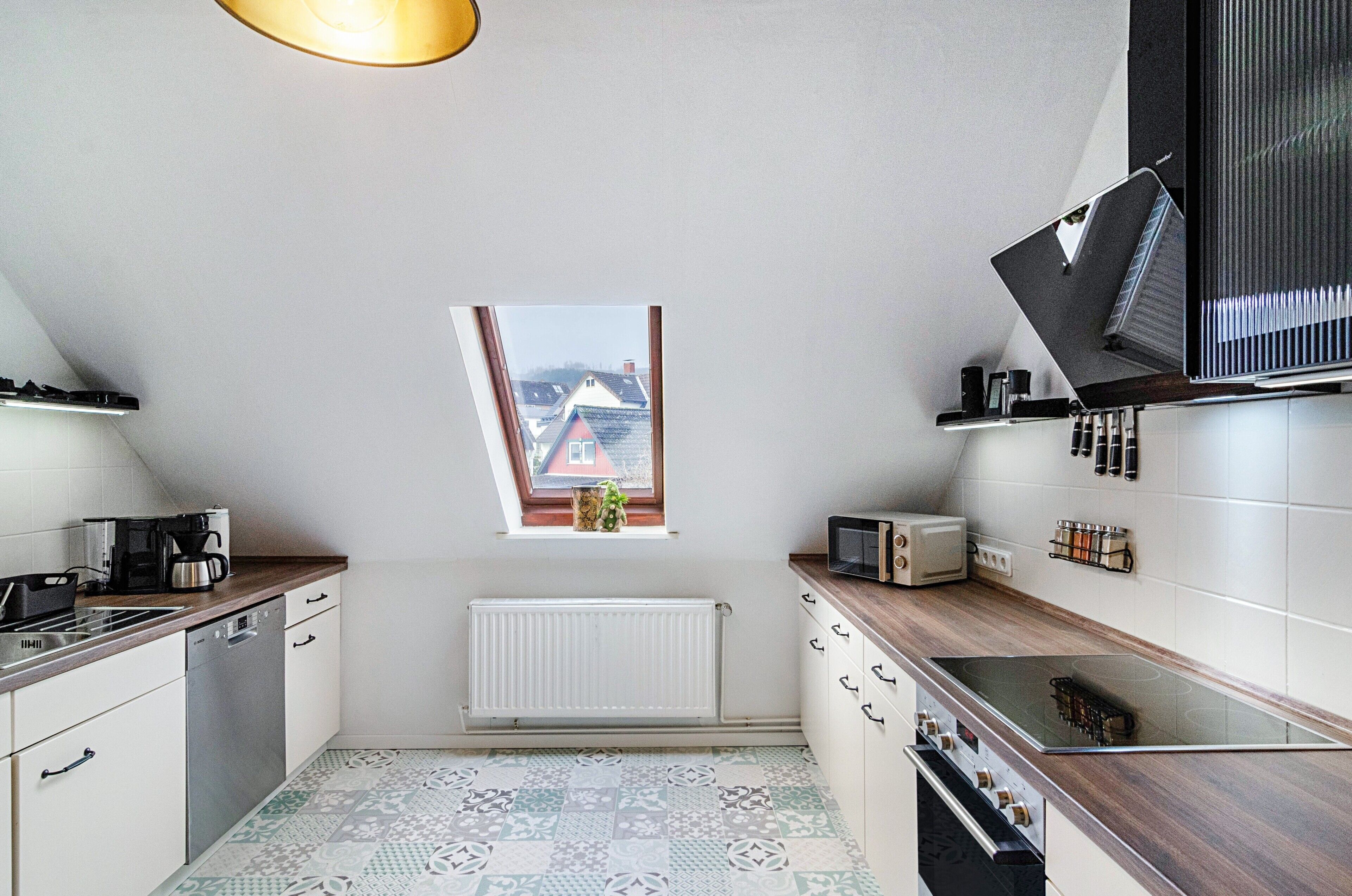 Een keuken met een raam, witte kastjes, een fornuis en een magnetron.