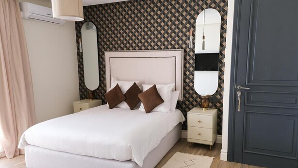 A neatly arranged bedroom with a large bed, two bedside tables, a dresser, and a dark door. - Villa Syria Luxe à Marrakech (Marrakech)