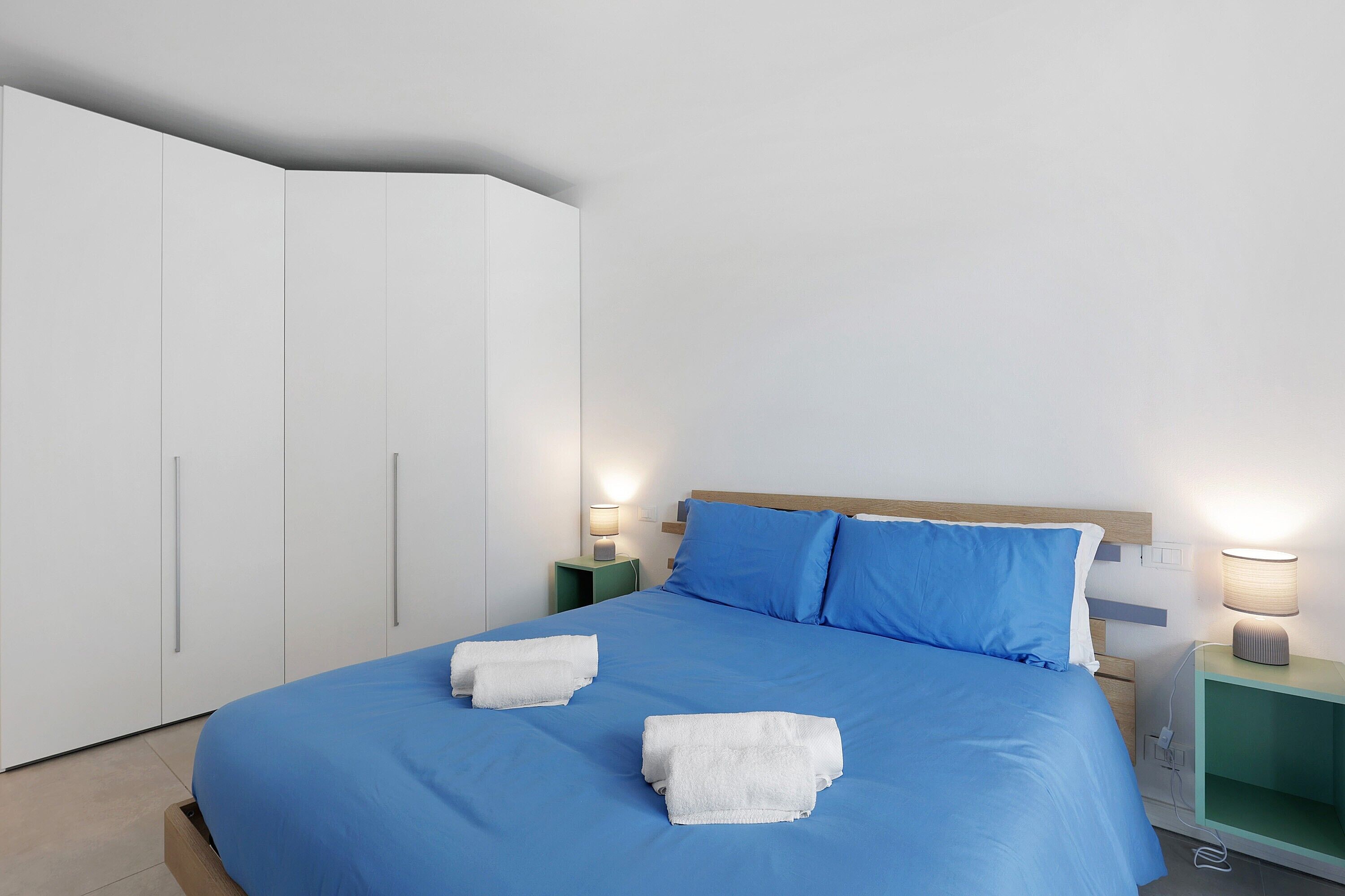A hotel room with a bed, two nightstands, a wardrobe, and a lamp.