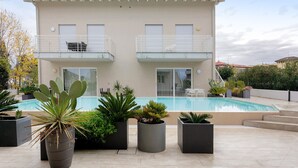Un bâtiment à deux étages doté d’une piscine, de plantes en pot et d’un balcon avec une chaise.