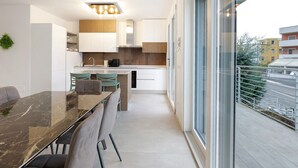 Une cuisine moderne dotée d’un plan de travail en marbre, d’un coin repas avec une table en verre et d’une vue sur un balcon agrémenté de balustrades.