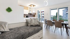 Une chambre moderne avec un lit, un coin repas avec des chaises, un espace cuisine et une vue dégagée sur l’extérieur grâce à de grandes fenêtres.