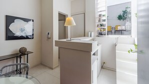 Une cuisine moderne avec un plan de travail blanc, une lampe et un coin repas comprenant une table en verre et des chaises en métal.