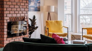 Ein gemütliches Wohnzimmer mit Kamin aus Ziegelsteinen, einem gelben Sessel und einem grünen Sofa.