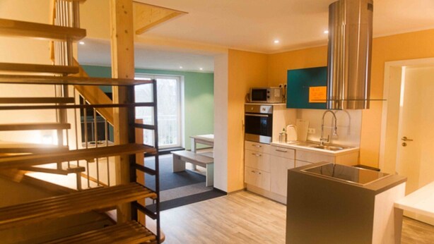 A modern kitchen with stainless steel appliances, a wooden staircase, and a view of the dining area.