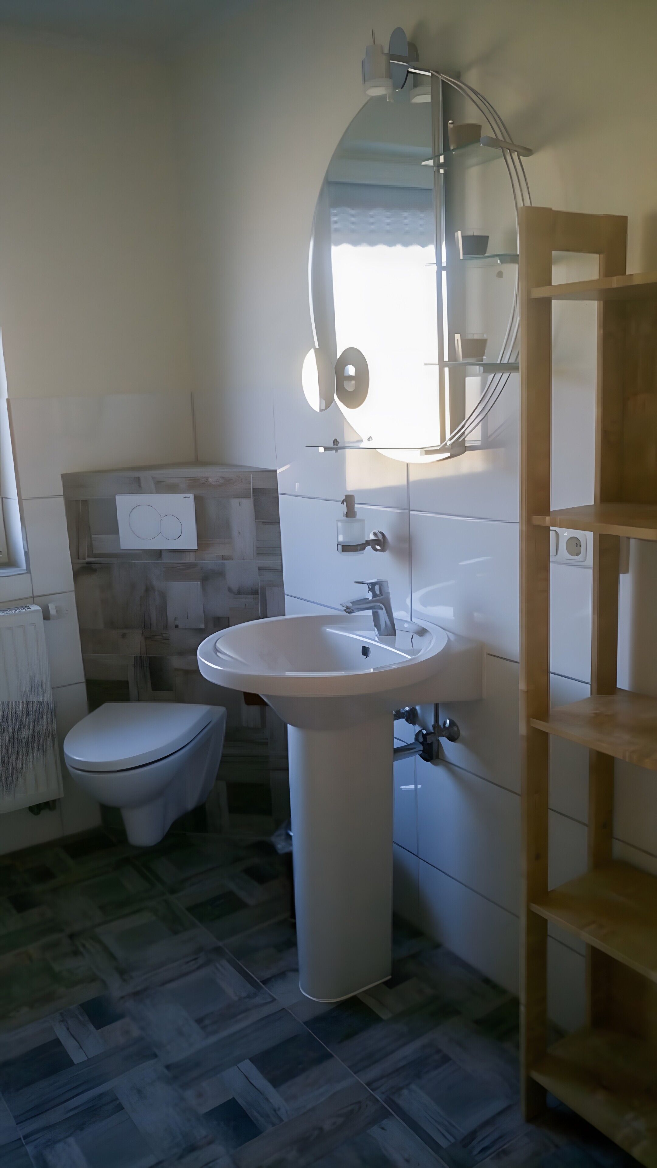 A bathroom with a toilet, sink, mirror, and a wooden shelf unit.