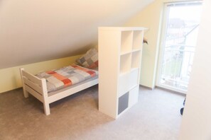 Ein kleines Zimmer mit einem Einzelbett, geneigter Decke und Fenster.