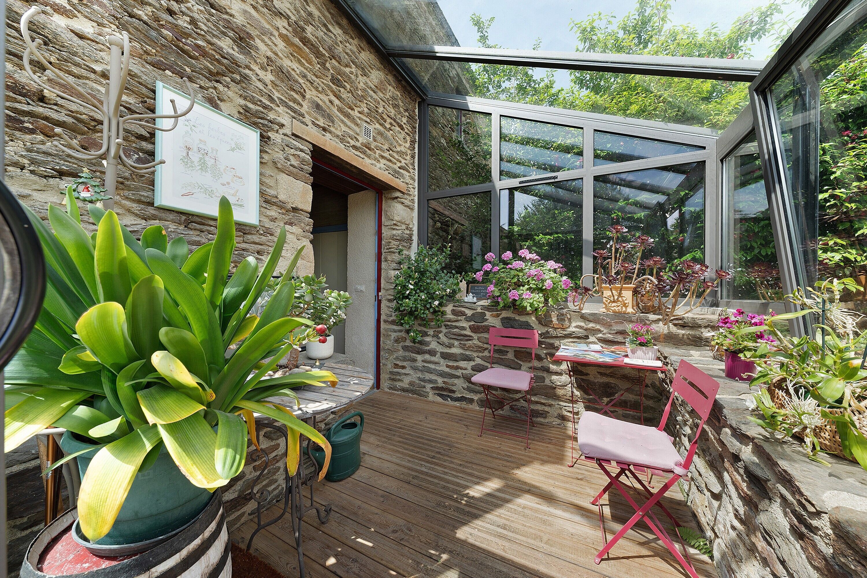 Une véranda avec un mur en pierre, une terrasse en bois et des plantes en pot.