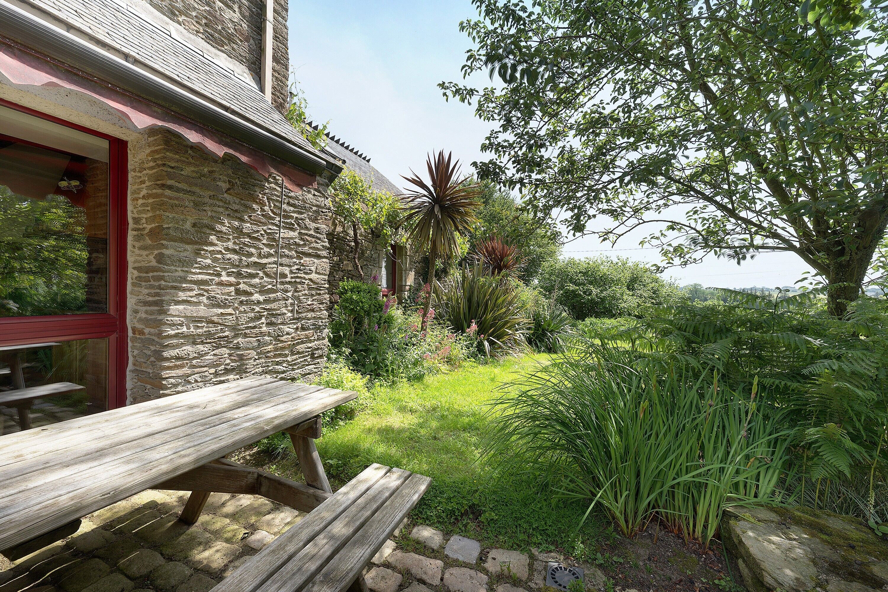 A stone building with a wooden bench and a garden with various plants.