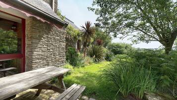 A stone building with a wooden bench and a garden with various plants.