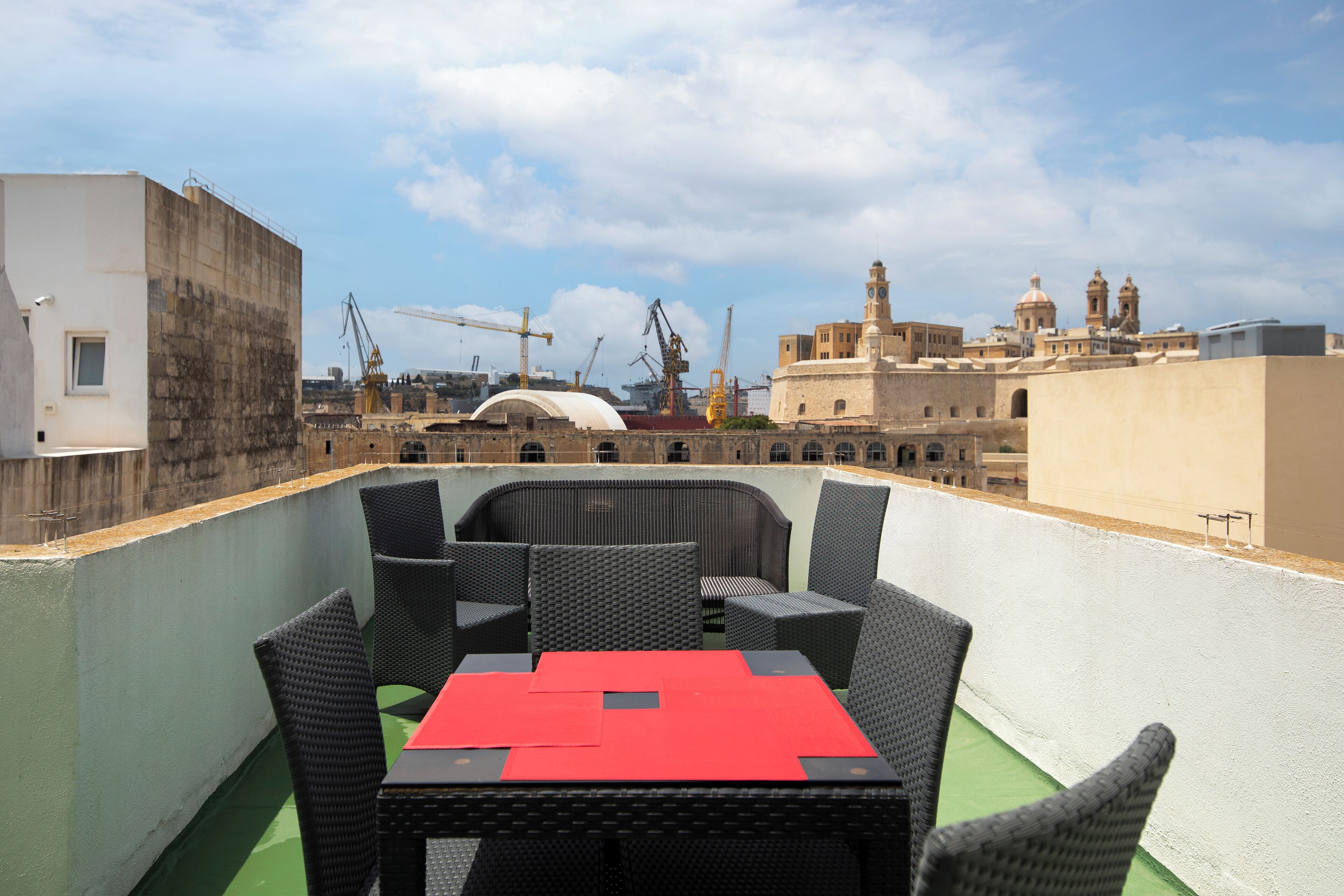Una terraza en la azotea con una mesa y sillas, vistas de la ciudad y grúas de construcción al fondo.