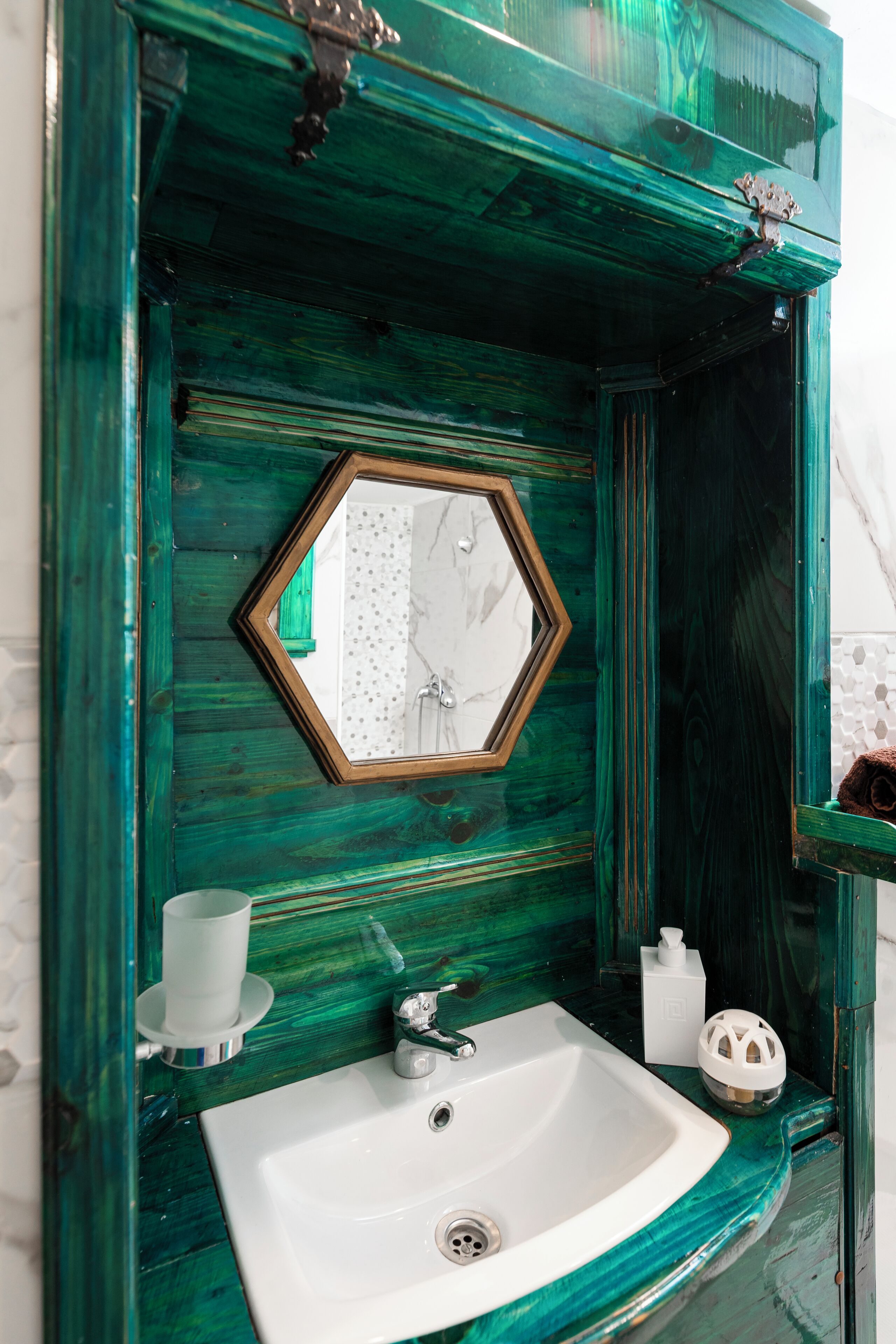 A bathroom with a green wooden vanity, a white sink, and a mirror with a hexagonal frame.