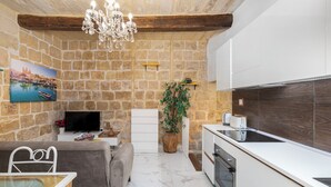 A modern kitchen with white cabinets, a built-in oven, and a stone wall backdrop. - Traditional Townhouse - Rooftop Seaviews (Cospicua)