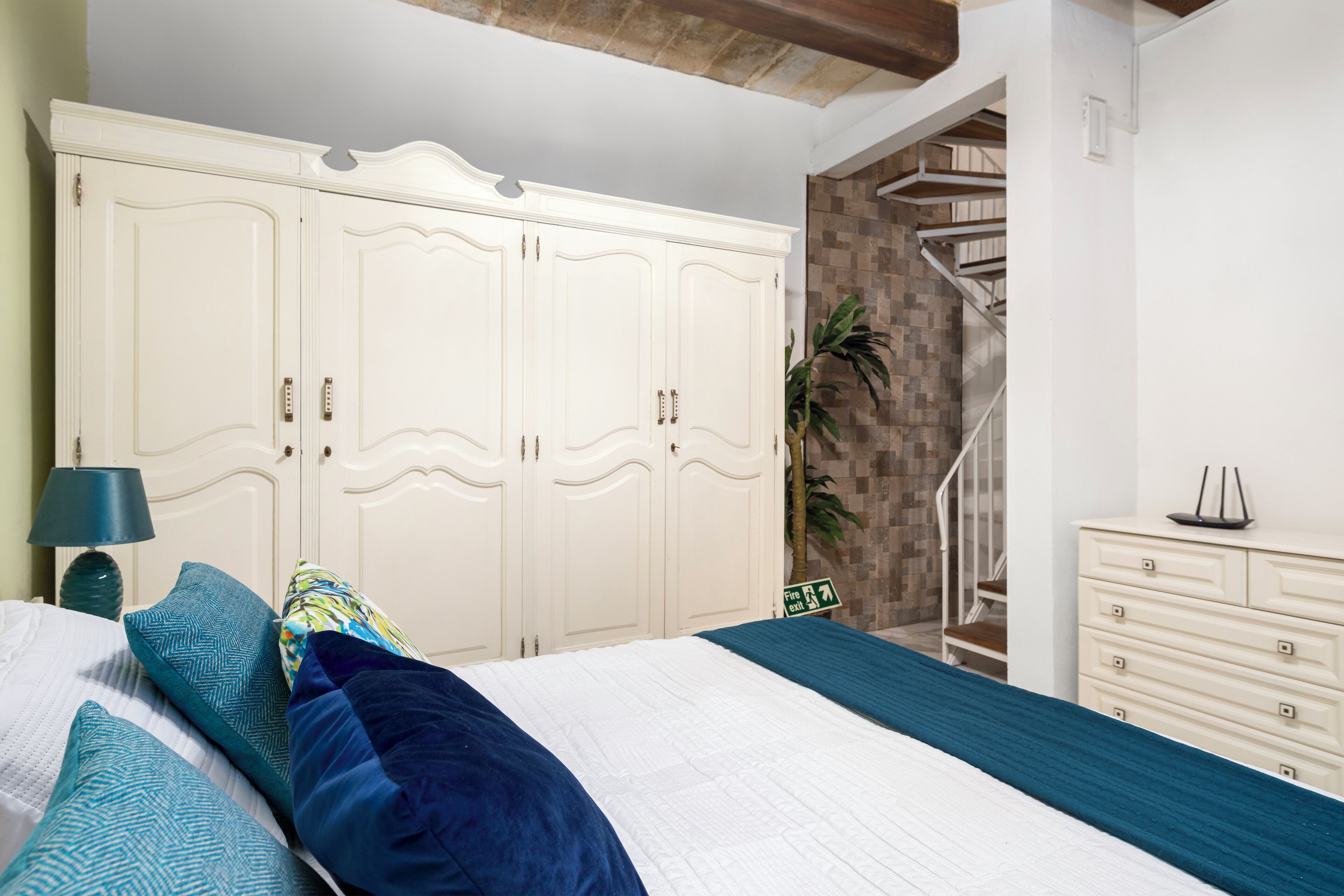 A bedroom with a bed, a wardrobe, a dresser, and a staircase.