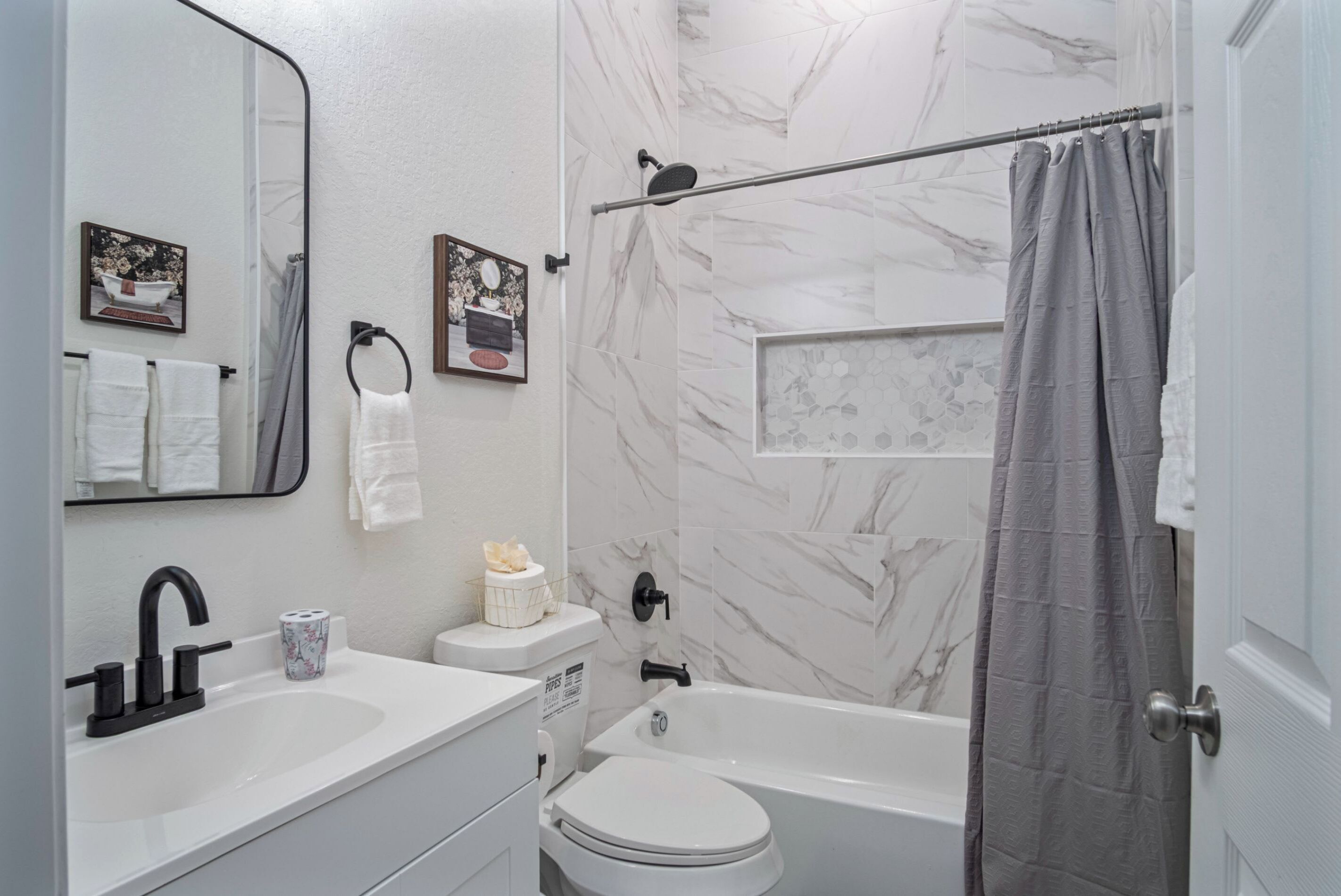 Ein Badezimmer mit weißem Waschbecken, WC und Badewanne. Handtücher hängen an der Wand und eine Duschvorhang ist angebracht.