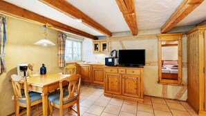 A kitchen with wooden cabinets, a dining table with chairs, a coffee maker, and a television. - Apartment "Linde" with Shared Garden and Wi-Fi (Sasbachwalden)