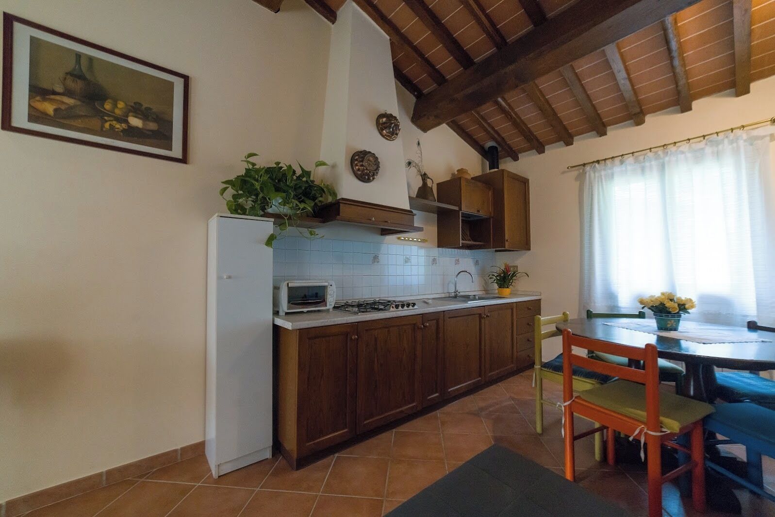 Une cuisine avec des meubles de rangement en bois, un réfrigérateur blanc, un four à micro-ondes et une cuisinière. On y trouve une table à manger avec des chaises et une fenêtre avec des rideaux.
