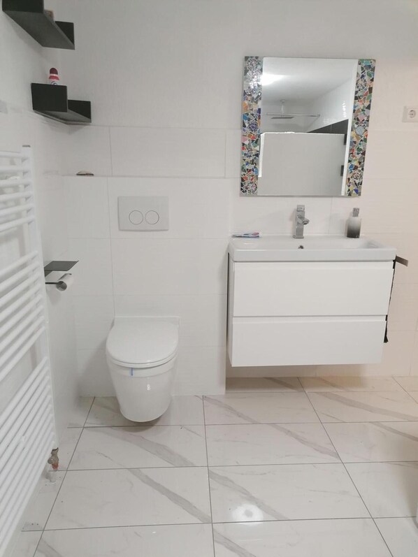 A bathroom with a toilet, a sink with a mirror, and a tiled floor.
