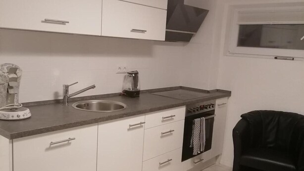 Een moderne keuken met witte kasten, een roestvrijstalen spoelbak, een koffiezetapparaat en een vaatwasser.