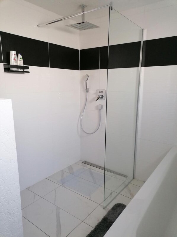 Una ducha con cerramiento de vidrio, cabezal de ducha manual y llave de pared.