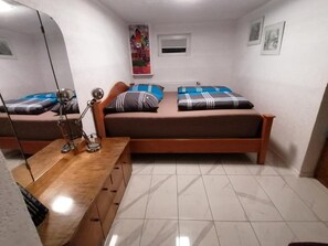 Una habitación pequeña y limpia con dos camas, un escritorio con lámpara, un espejo y una ventana.