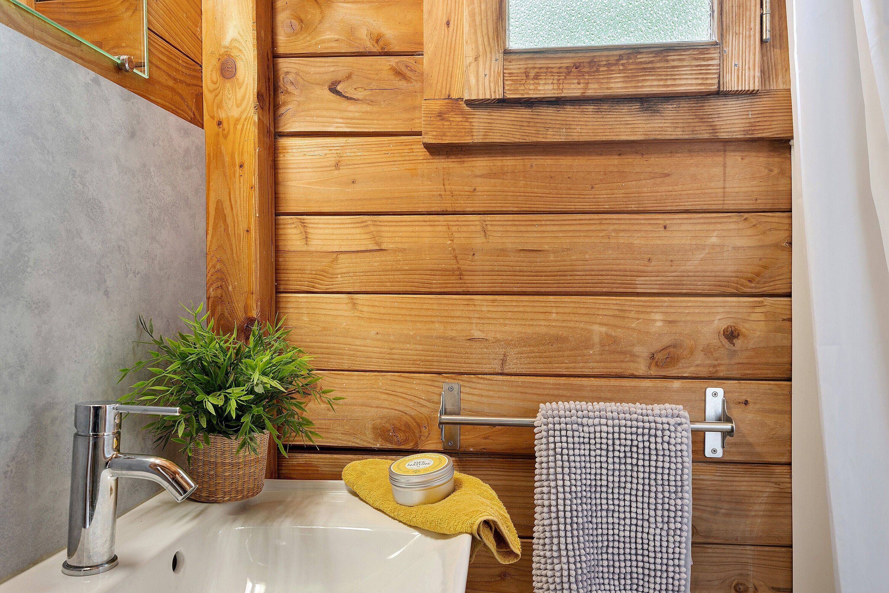 Un baño con pared de madera, un lavabo, un espejo, un perchero para toallas y una planta en maceta.