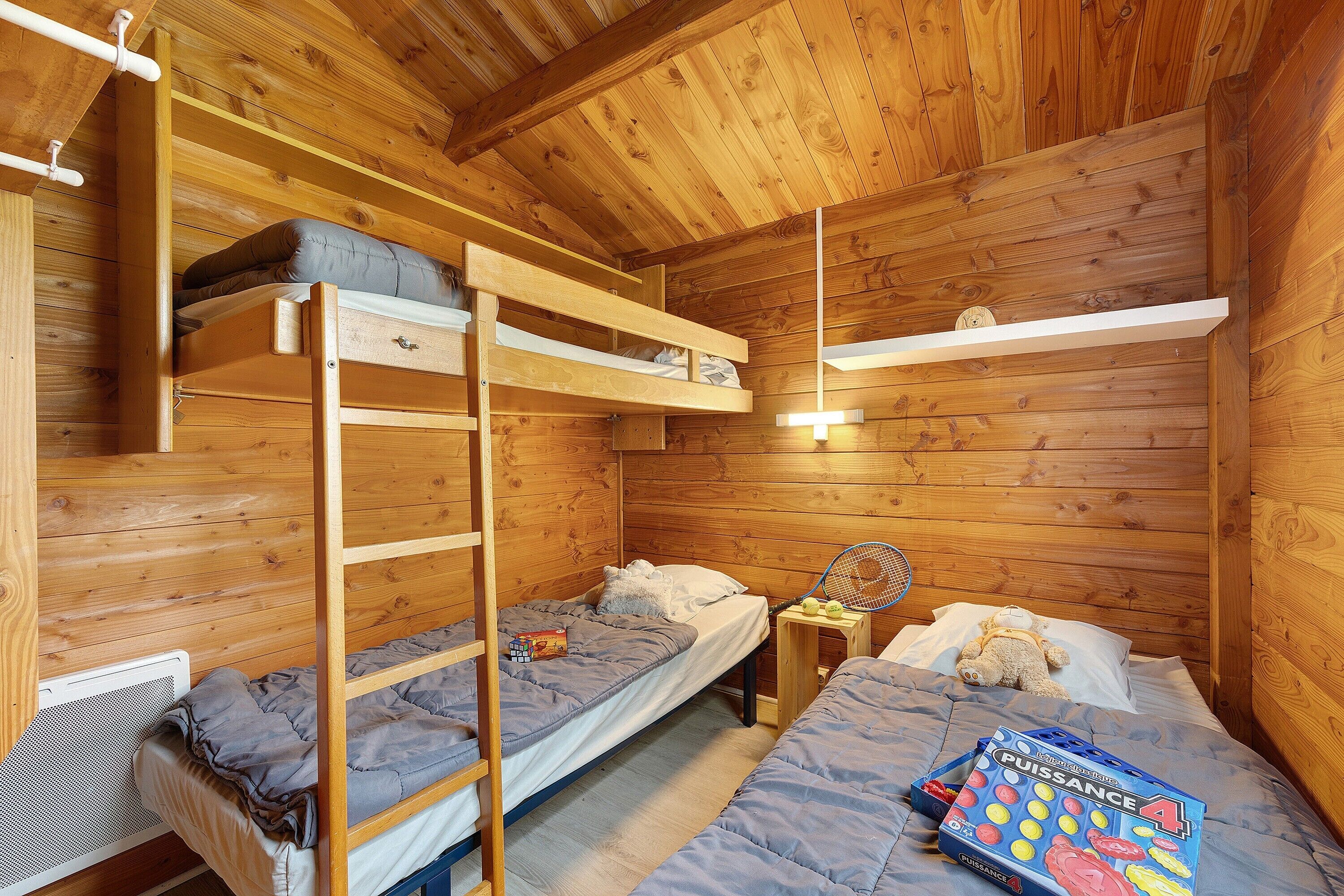 Une pièce de cabane en bois avec des lits superposés, une échelle, une petite table et un livre.