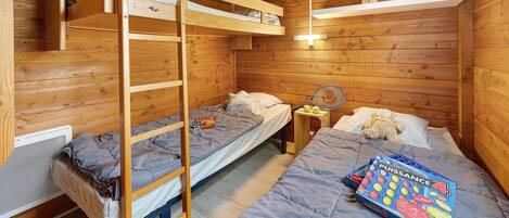 Une pièce de cabane en bois avec des lits superposés, une échelle, une petite table et un livre.