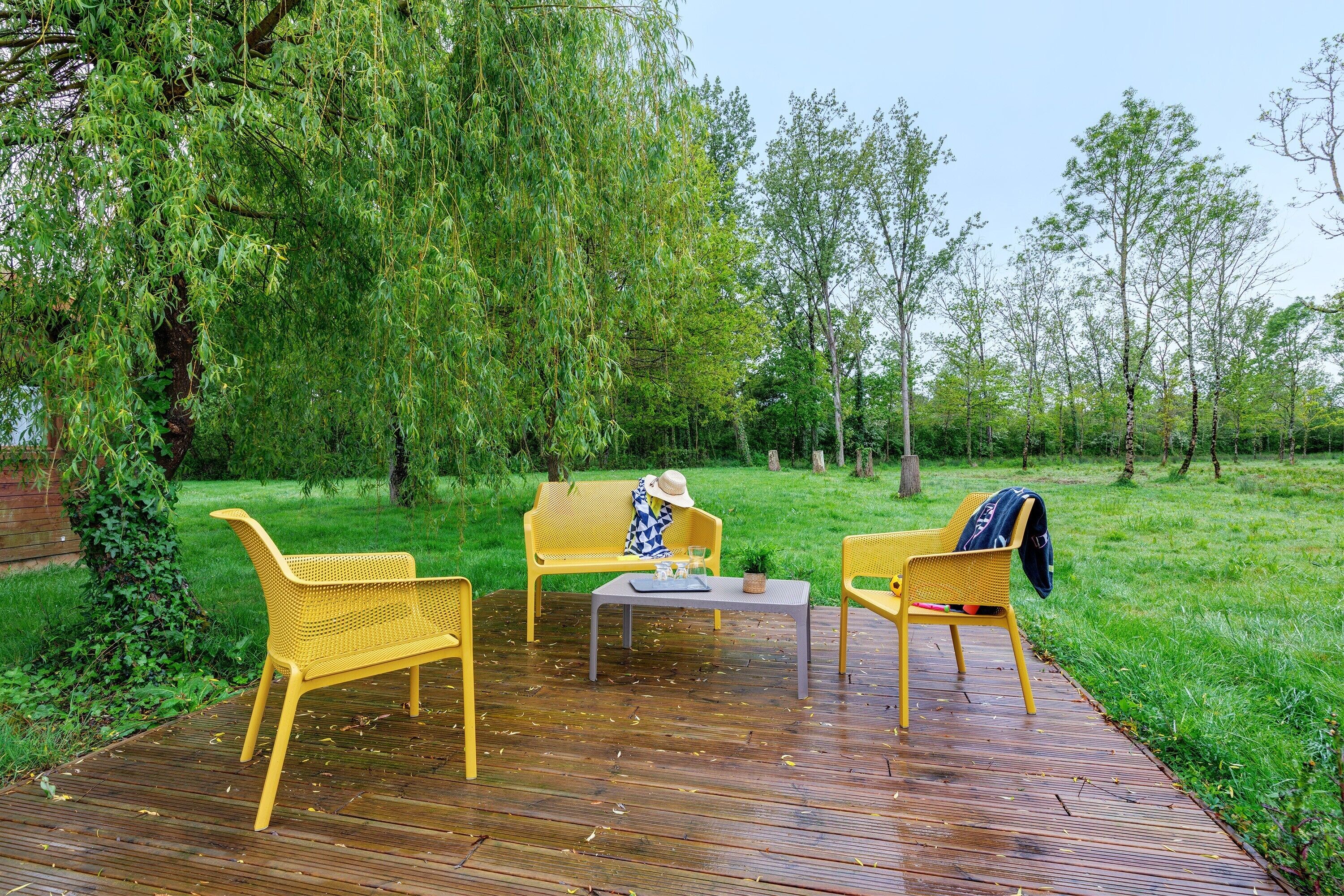 Une terrasse en bois avec des meubles en osier jaune, une petite table et un banc.