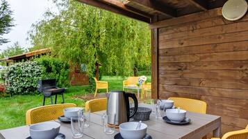 Een buiten eethoek met een tafel voor vier personen, omringd door gele stoelen, een metalen waterkoker en glazen.